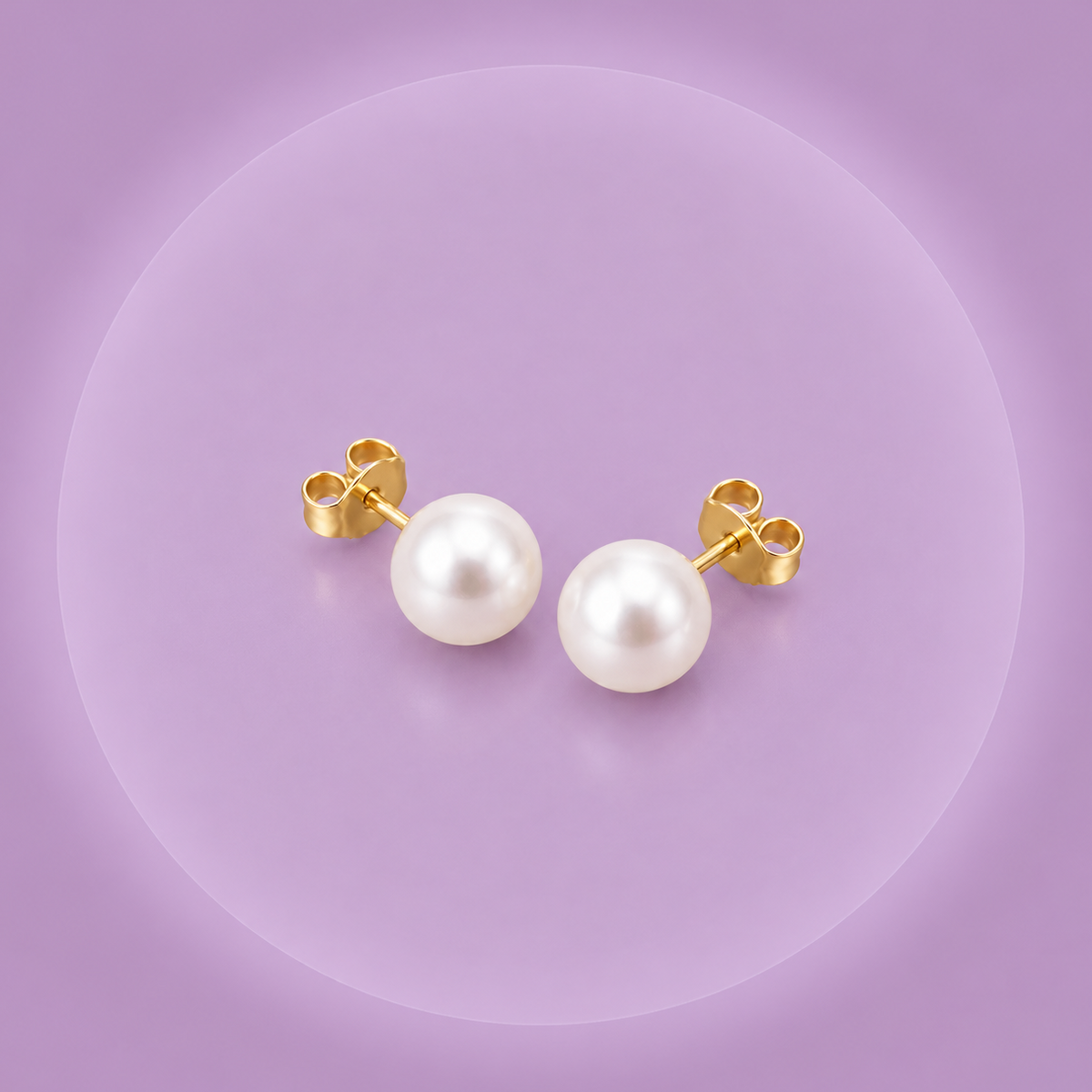 Paire de boucles d'oreilles clous en perle de culture blanche, monture plaqué or 18K, posées sur fond violet