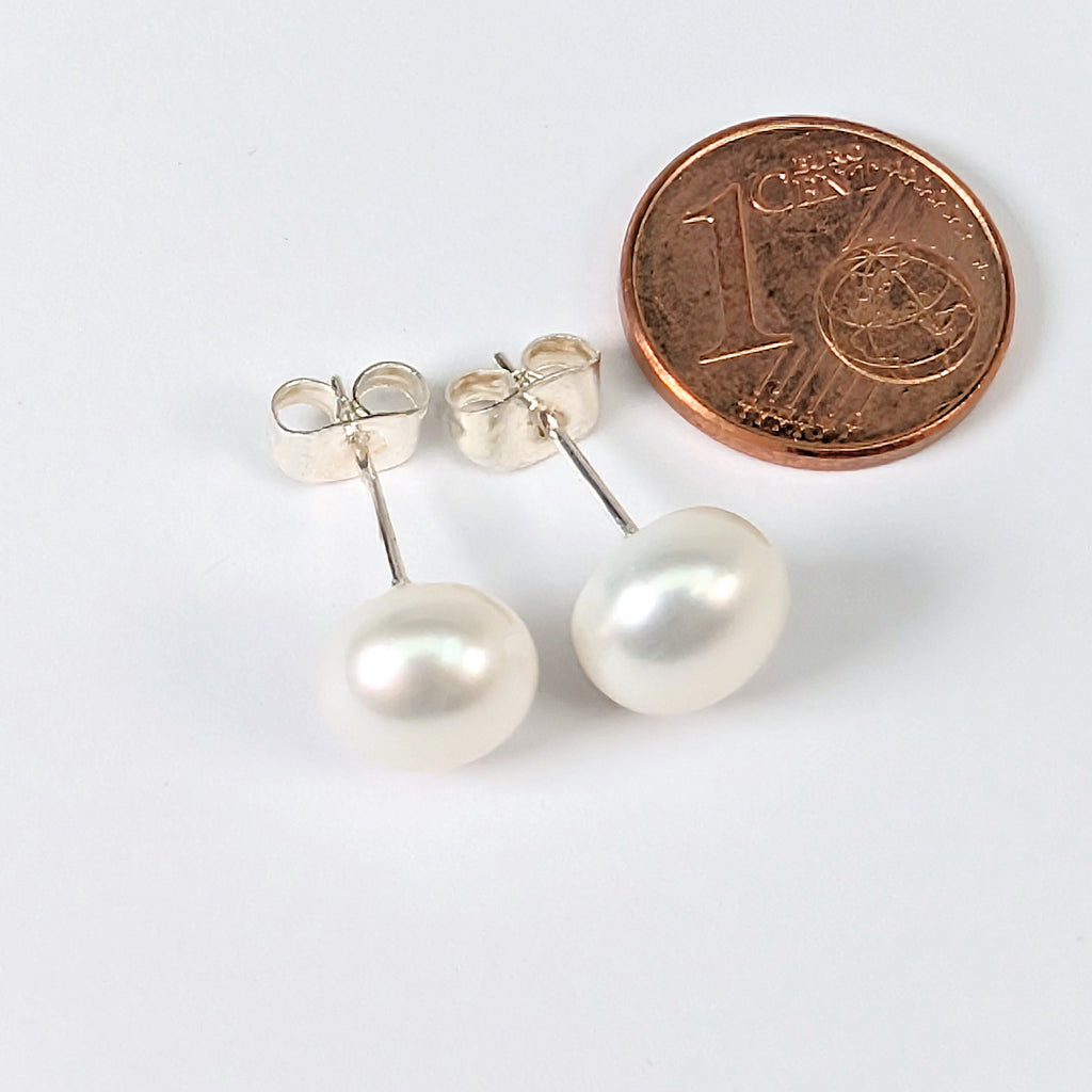 Paire de boucles d'oreilles Diana en perle de culture blanche de 8mm, monture clou en argent 925, posées à côté d'une pièce de 1 centime pour comparer la taille