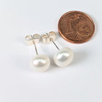 Paire de boucles d'oreilles Diana en perle de culture blanche de 8mm, monture clou en argent 925, posées à côté d'une pièce de 1 centime pour comparer la taille