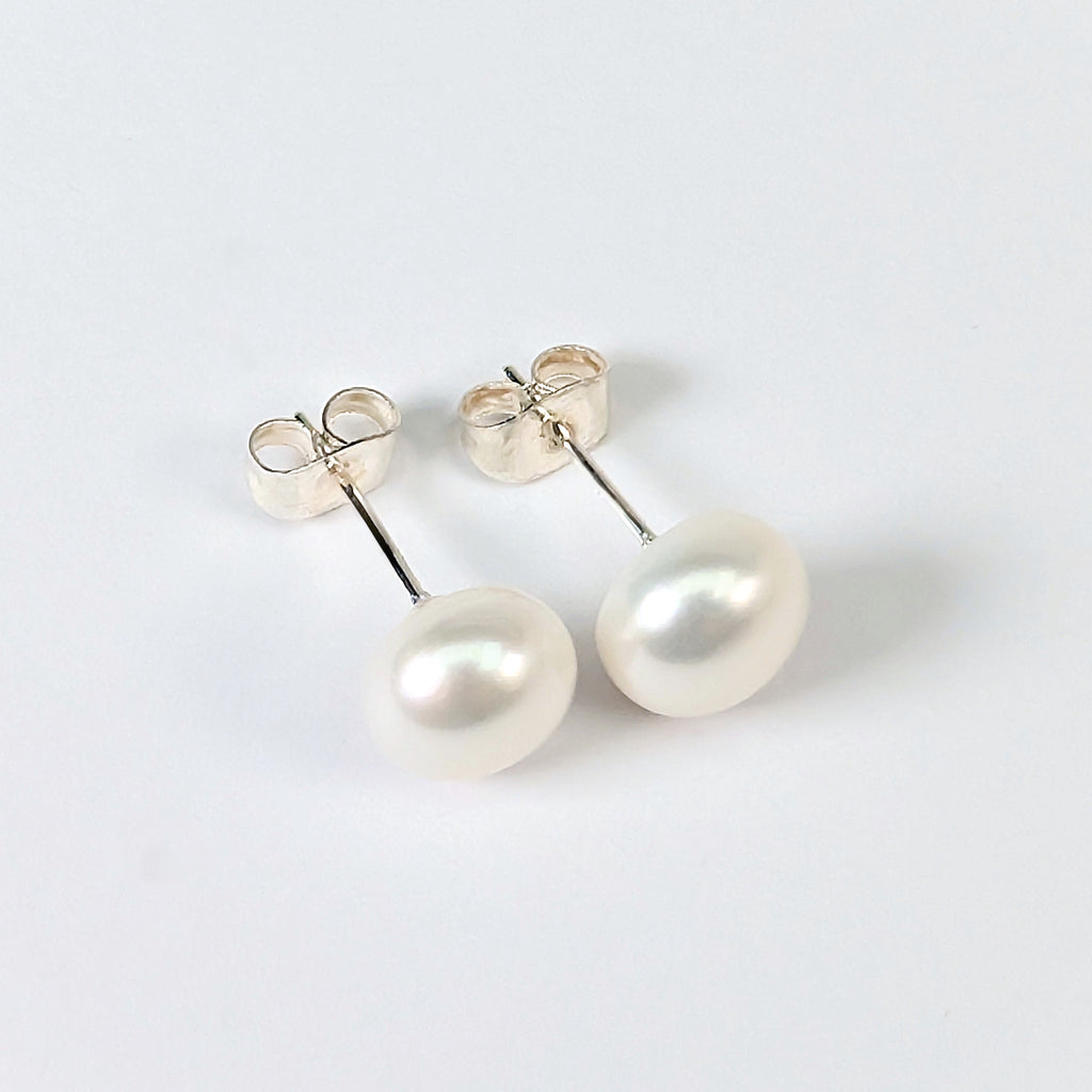 Paire de boucles d'oreilles Diana posées à plat côte à côte sur fond blanc, clous en argent 925 surmontés chacun d'une perle de culture blanche en forme de bouton de 8mm