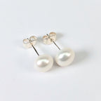 Paire de boucles d'oreilles Diana posées à plat côte à côte sur fond blanc, clous en argent 925 surmontés chacun d'une perle de culture blanche en forme de bouton de 8mm