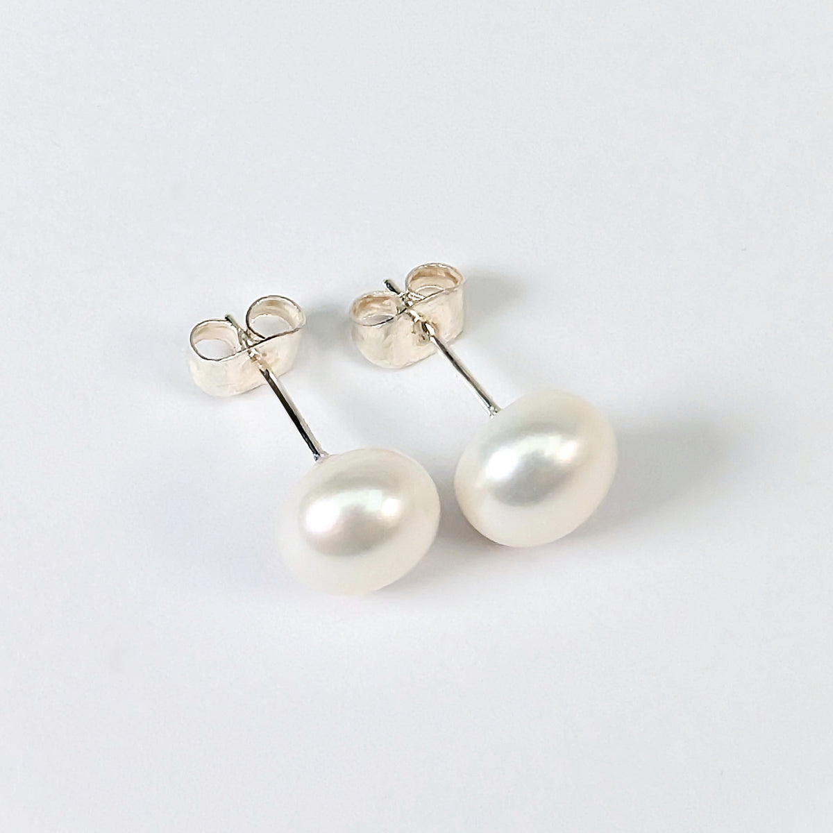 Paire de boucles d'oreilles Diana posées à plat côte à côte sur fond blanc, clous en argent 925 surmontés chacun d'une perle de culture blanche en forme de bouton de 8mm