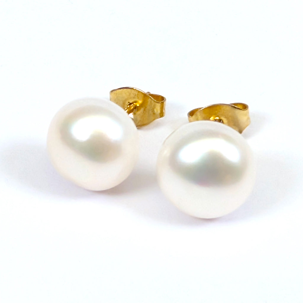 Paire de boucles d'oreilles Diana posées à plat côte à côte sur fond blanc, clous en plaqué or 18K surmontés chacun d'une perle de culture blanche en forme de bouton