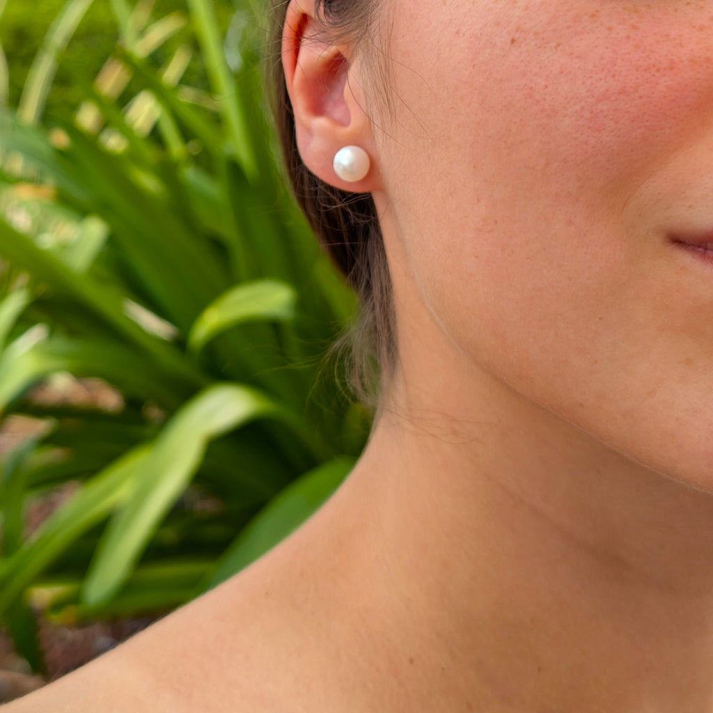 Boucle d'oreille Diana portée, vue de trois-quarts, clou doré et perle blanche en forme de bouton, nacrée, visibles contre la peau et les cheveux