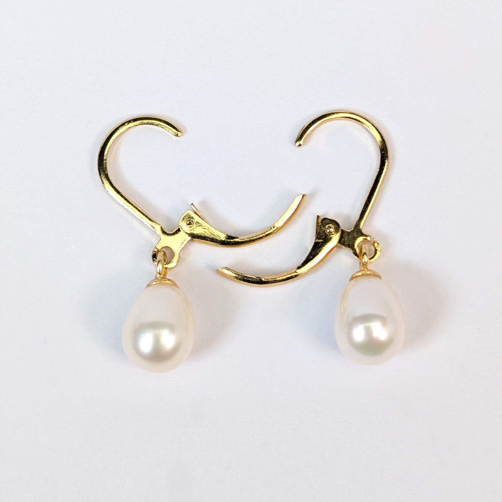 Gros plan sur une boucle d'oreille Aphrodite, fermoir dormeuse en plaqué or 18K et perle blanche en forme de goutte d'eau, fond blanc uni