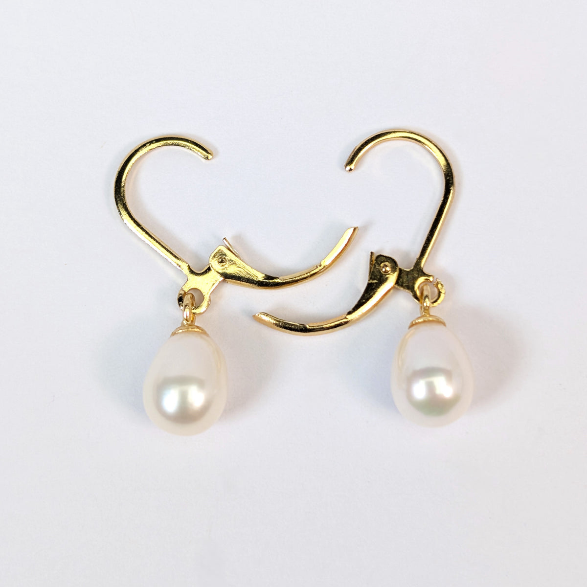 Gros plan sur une boucle d'oreille Aphrodite, fermoir dormeuse en plaqué or 18K et perle blanche en forme de goutte d'eau, fond blanc uni