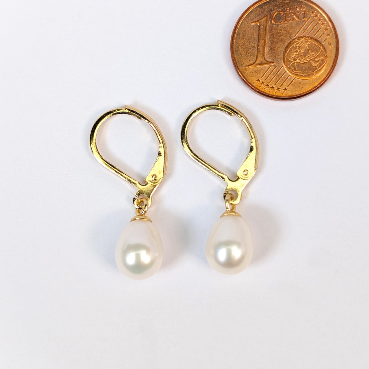 Boucles d'oreilles Aphrodite à côté d'une pièce d'1 centime pour comparaison de taille, perle de culture blanche en forme de goutte d'eau
