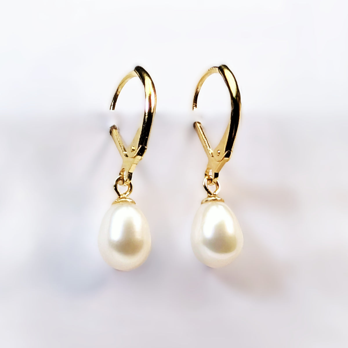 Paire de boucles d'oreilles Aphrodite suspendues, montrant la monture dormeuse en plaqué or 18K et la perle blanche ovale en forme de goutte d'eau