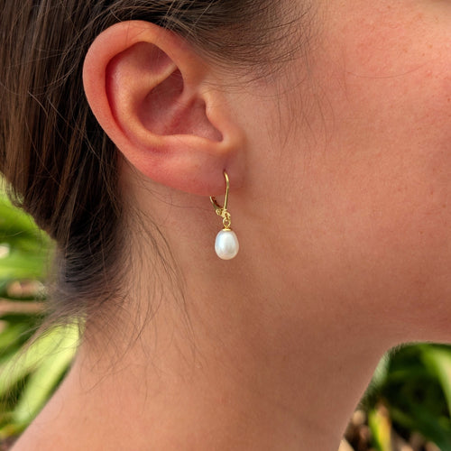 Femme portant une boucle d'oreille Aphrodite à l'oreille, monture dormeuse en plaqué or 18K et perle de culture blanche en forme de goutte d'eau, vue de profil