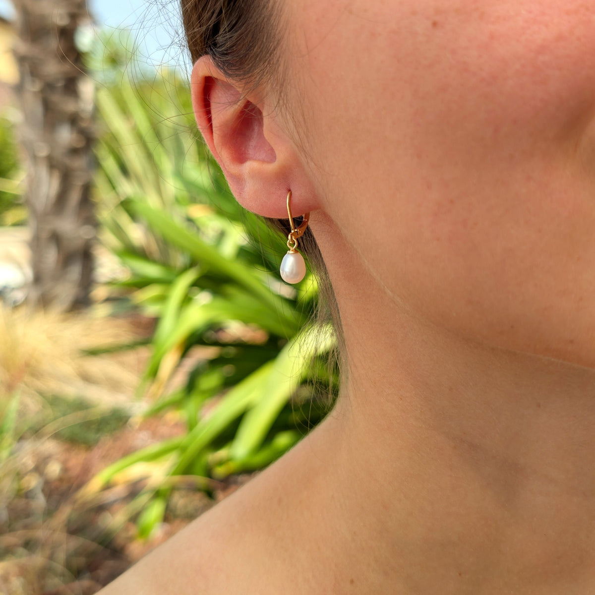 Boucle d'oreille Aphrodite portée, vue de trois-quarts, monture dormeuse dorée et perle blanche ovale en forme de goutte d'eau