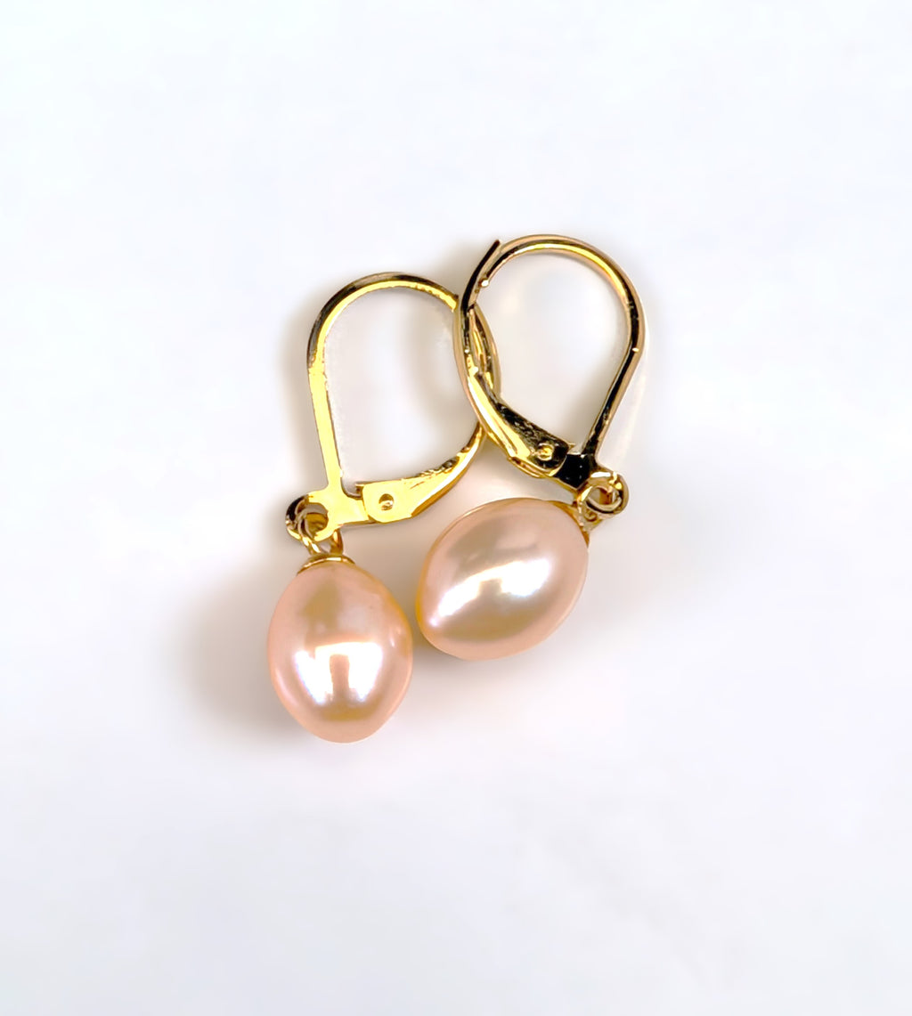 Gros plan sur une boucle d'oreille Aphrodite, fermoir dormeuse en plaqué or 18K et perle rose en forme de goutte d'eau, fond blanc uni