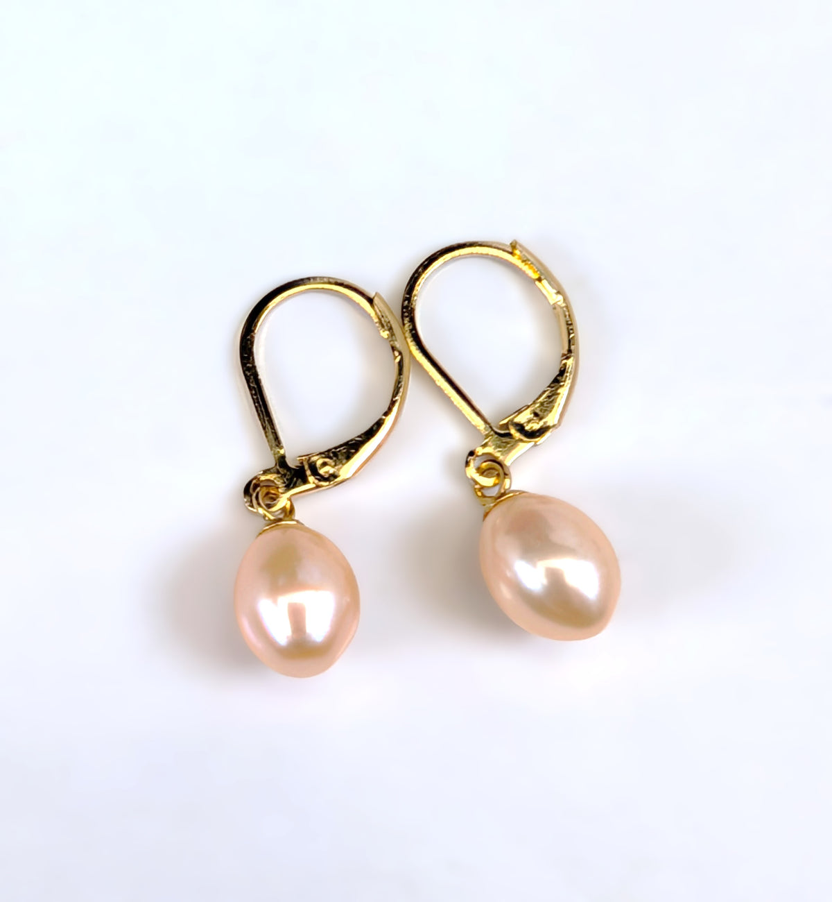 Paire de boucles d'oreilles Aphrodite posées à plat côte à côte sur fond blanc, montures dormeuses en plaqué or 18K et perles roses en forme de goutte d'eau