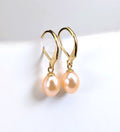 Paire de boucles d'oreilles Aphrodite suspendues, montrant la monture dormeuse en plaqué or 18K et la perle rose ovale en forme de goutte d'eau