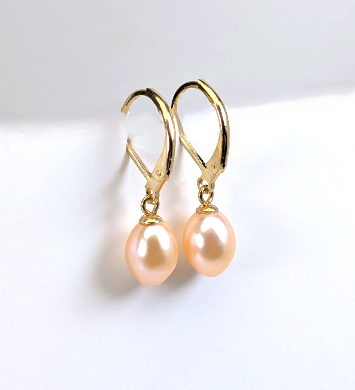 Paire de boucles d'oreilles Aphrodite suspendues, montrant la monture dormeuse en plaqué or 18K et la perle rose ovale en forme de goutte d'eau