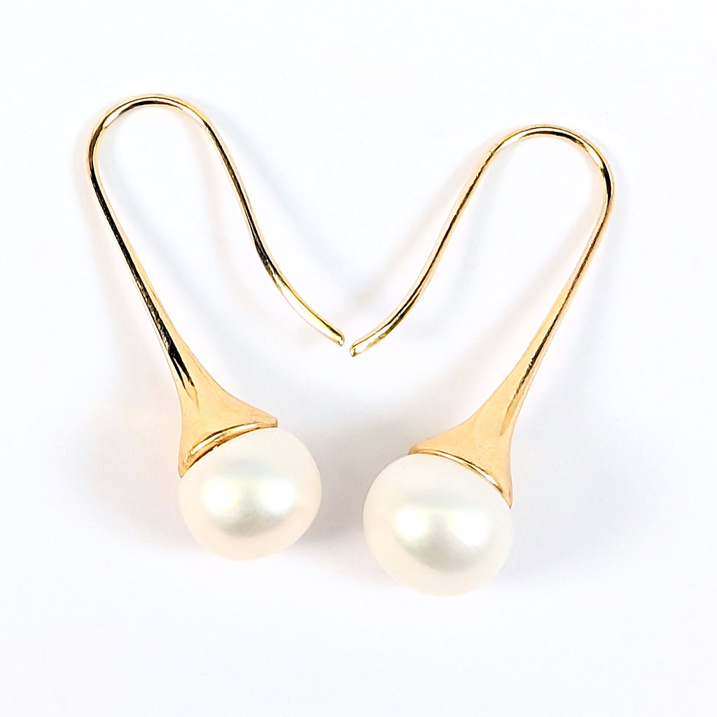 Gros plan sur une boucle d'oreille Aurore, monture pendante en plaqué or 18K et perle blanche en forme de bouton, fond blanc uni