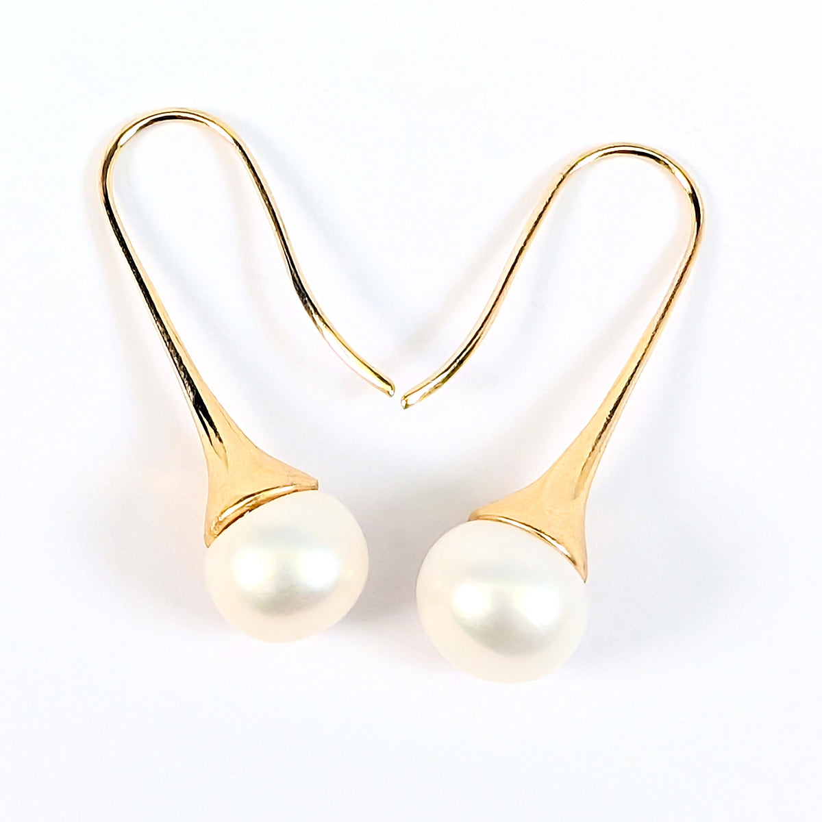 Gros plan sur une boucle d'oreille Aurore, monture pendante en plaqué or 18K et perle blanche en forme de bouton, fond blanc uni