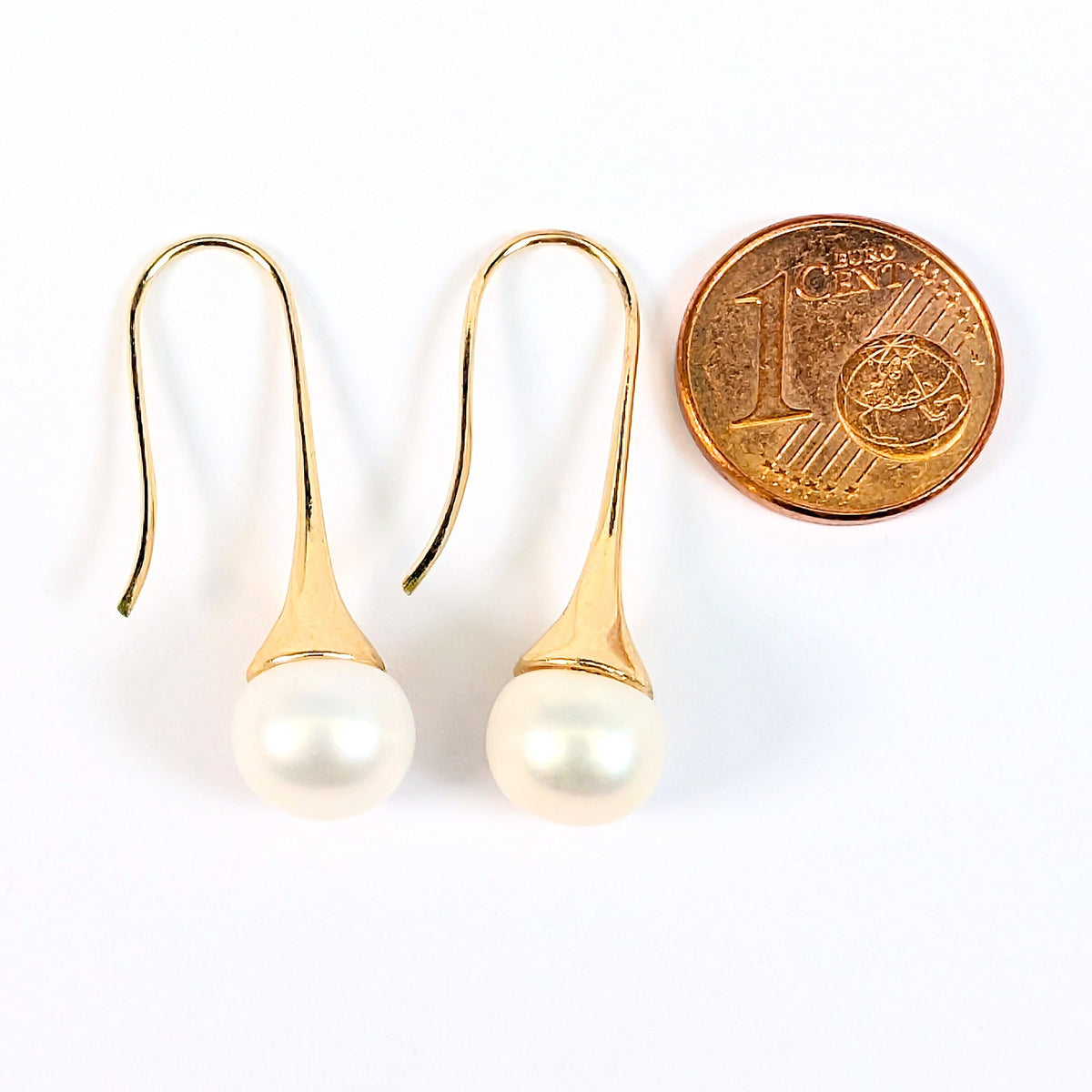 Boucles d'oreilles Aurore à côté d'une pièce d'1 centime pour comparaison de taille, perle de culture blanche en forme de bouton