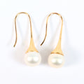 Paire de boucles d'oreilles Aurore posées à plat côte à côte sur fond blanc, montures pendantes en plaqué or 18K et perles blanches en forme de bouton