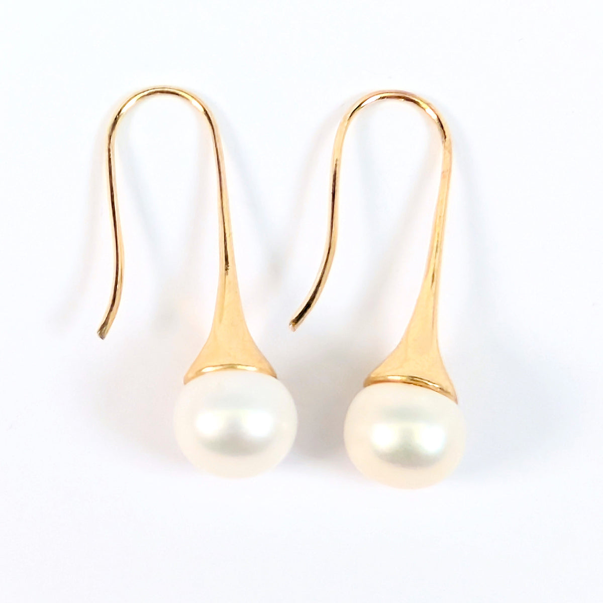 Paire de boucles d'oreilles Aurore posées à plat côte à côte sur fond blanc, montures pendantes en plaqué or 18K et perles blanches en forme de bouton