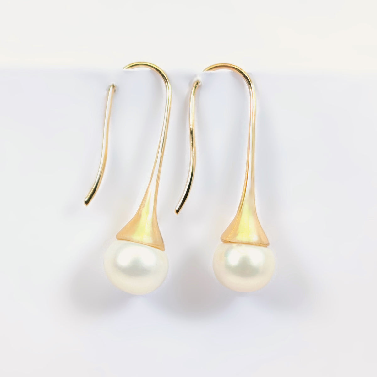 Paire de boucles d'oreilles Aurore suspendues, montrant la monture pendante en plaqué or 18K et la perle blanche en forme de bouton