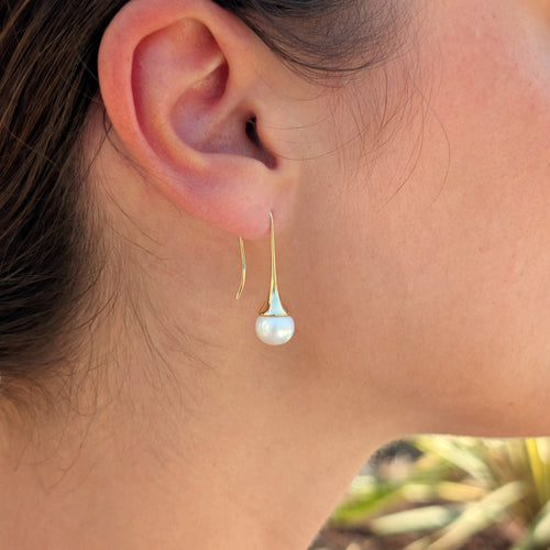 Femme portant une boucle d'oreille Aurore à l'oreille, monture pendante en plaqué or 18K et perle blanche en forme de bouton, vue de profil