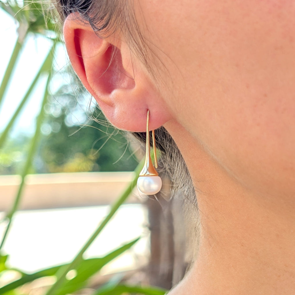 Boucle d'oreille Aurore portée, vue de trois-quarts, monture pendante dorée et perle blanche en forme de bouton