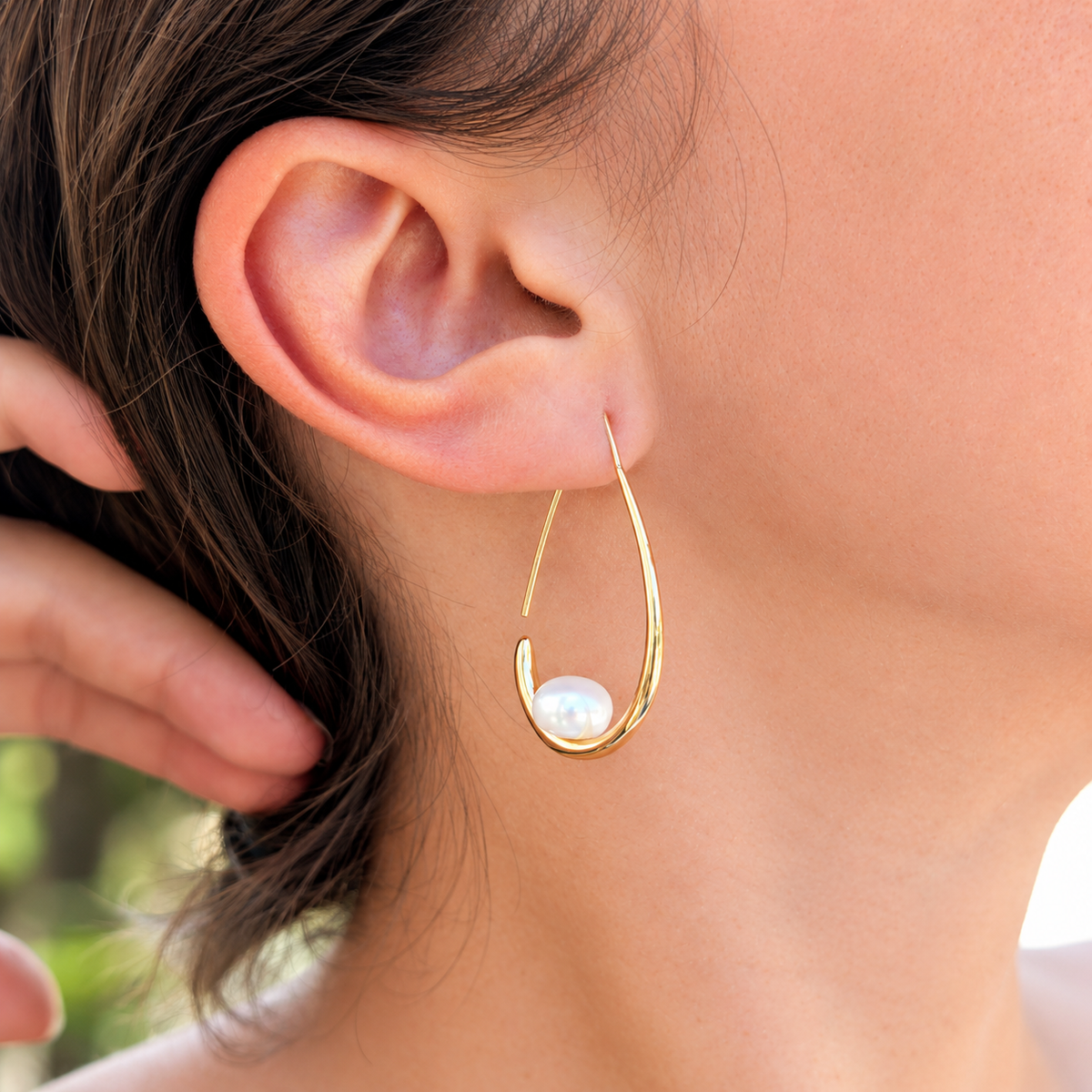Boucle d'oreille Calypso portée, vue de trois-quarts, monture pendante dorée et perle blanche en forme de bouton