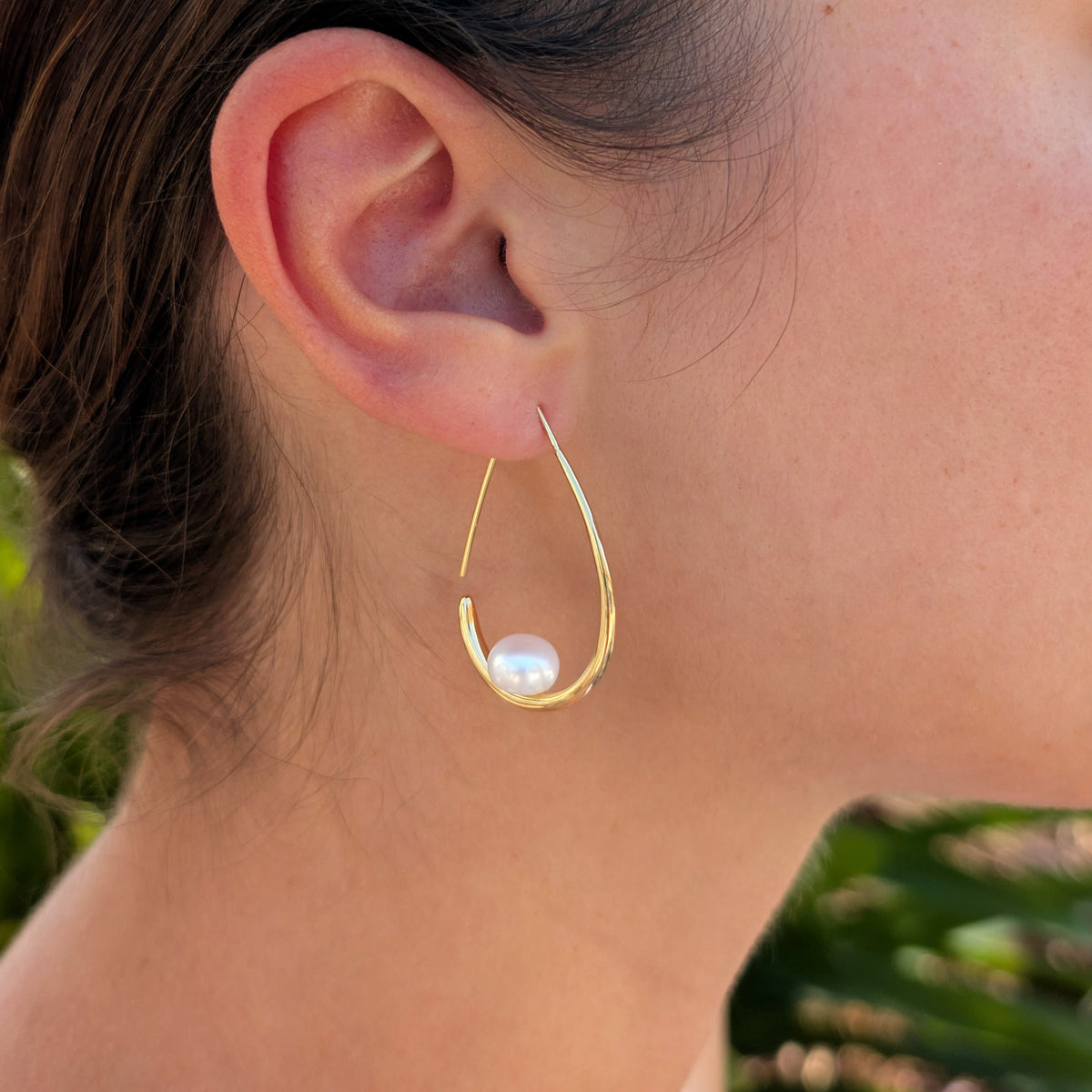 Femme portant une boucle d'oreille Calypso à l'oreille, monture pendante ouverte en plaqué or 18K et perle blanche en forme de bouton, vue de profil