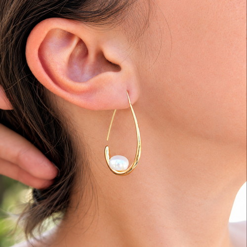 Boucle d'oreille Calypso portée, vue de trois-quarts, monture pendante ouverte en plaqué or 18K et perle de culture blanche en forme de bouton de 8mm