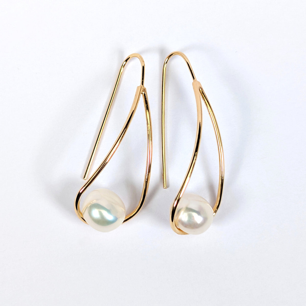 Paire de boucles d'oreilles Sissi posées à plat côte à côte sur fond blanc, montures pendantes en plaqué or 18K et perles blanches en forme de bouton