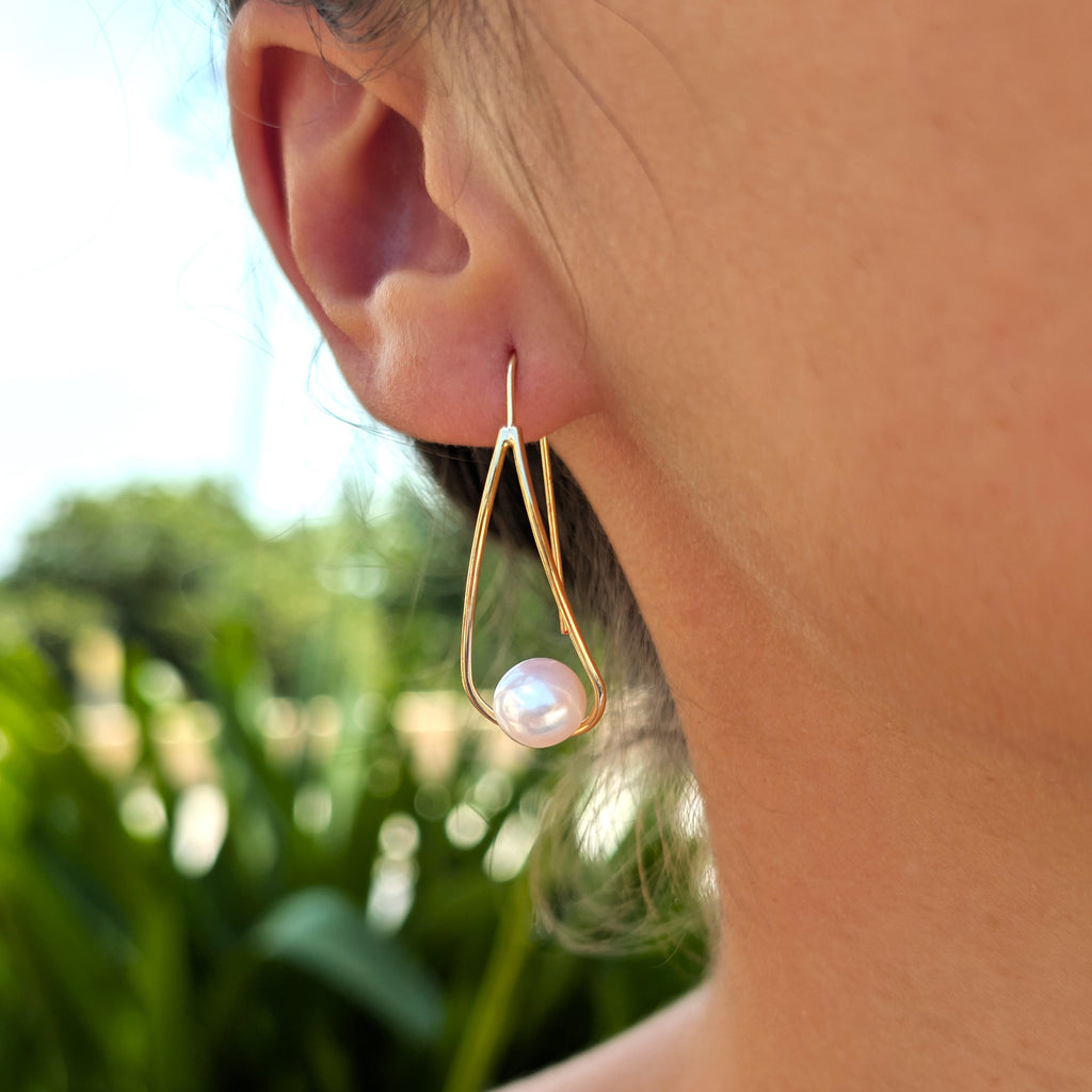 Boucle d'oreille Sissi portée, vue de trois-quarts, monture pendante dorée et perle blanche en forme de bouton