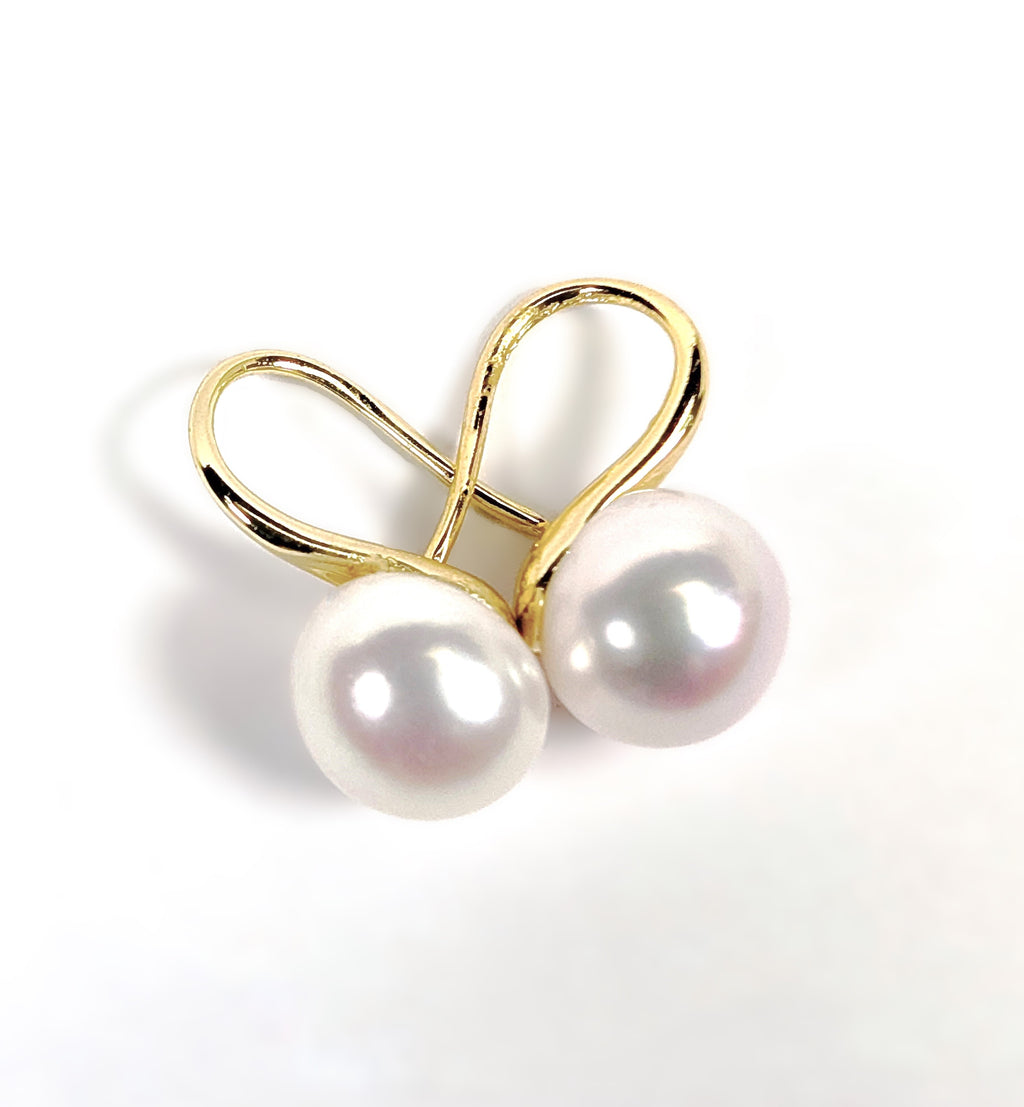 Gros plan sur une boucle d'oreille Cléopâtre, monture pendante en plaqué or 18K et perle blanche en forme de bouton, fond blanc uni