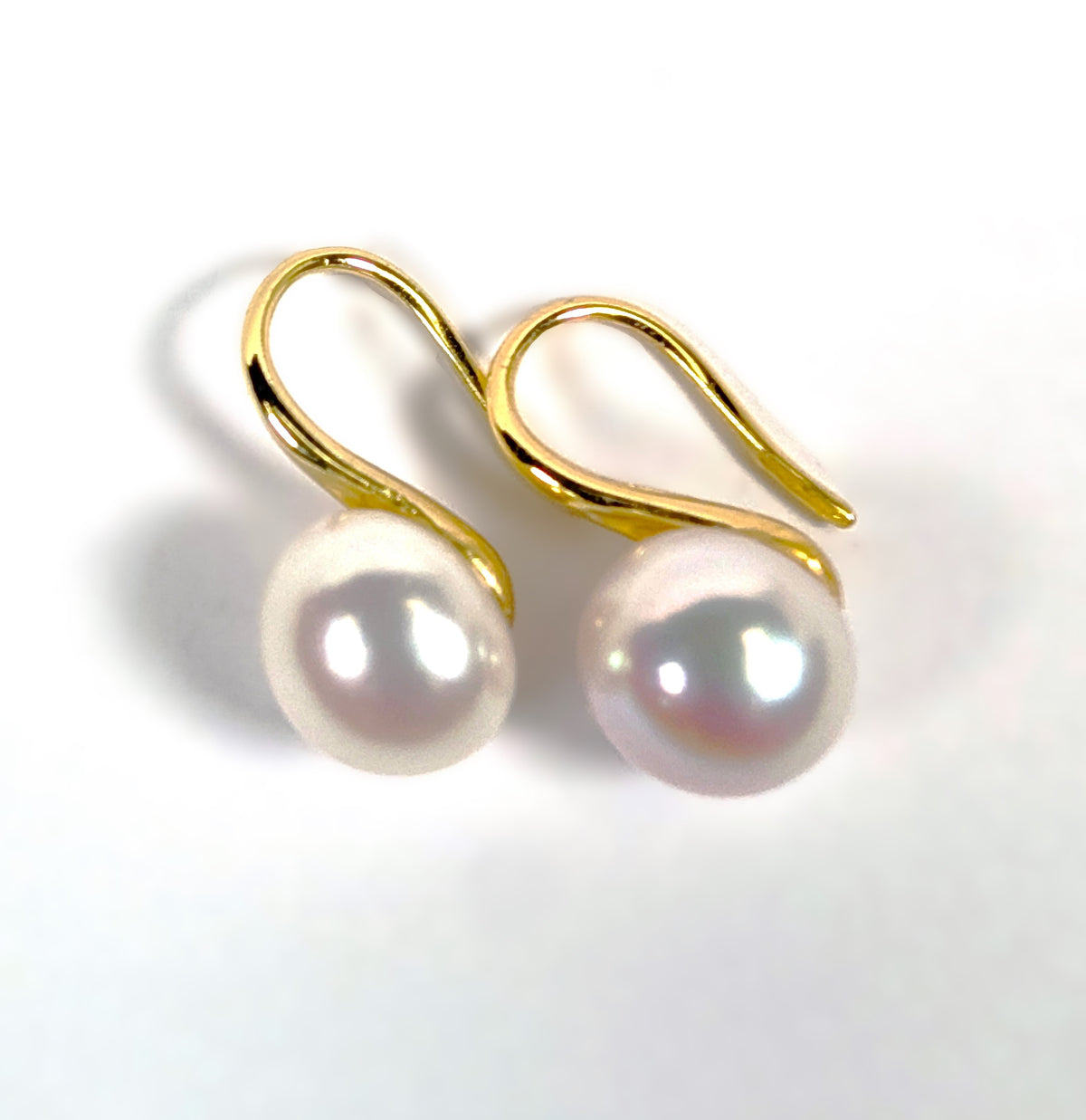 Paire de boucles d'oreilles Cléopâtre posées à plat côte à côte sur fond blanc, montures pendantes en plaqué or 18K et perles blanches en forme de bouton
