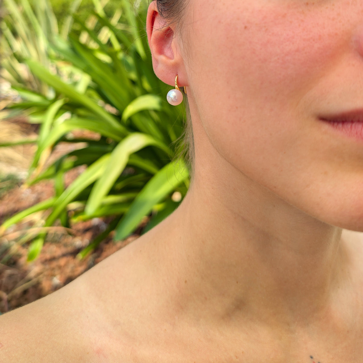 Boucle d'oreille Cléopâtre portée, vue de trois-quarts, monture pendante dorée et perle blanche en forme de bouton